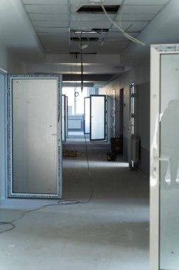 Yeni bir binanın boş koridorunda inşaat devam ediyor. İnşaat altındaki bir binanın geniş koridorunda çerçeveli kapılar ve inşaat elemanları görülüyor.