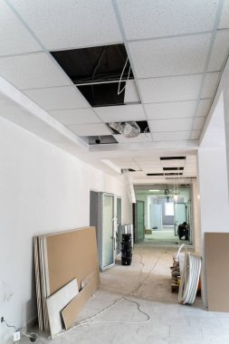 Tavanı düşmüş modern bir ofis koridorunda inşaat çalışmaları sürüyor. Çağdaş bir ofis koridorunda tavan elementleriyle tadilat başladı