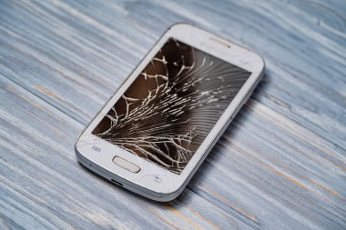 Hasarlı akıllı telefon ve kırık ekran ahşap masada duruyor. Paramparça bir ekranı olan akıllı bir telefon ahşap bir yüzeye uzanır.