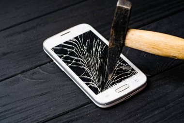 Tahta bir yüzeyde parçalanmış bir akıllı telefon ekranına çarpan bir çekiç. Bir çekiç akıllı telefona vuruyor.
