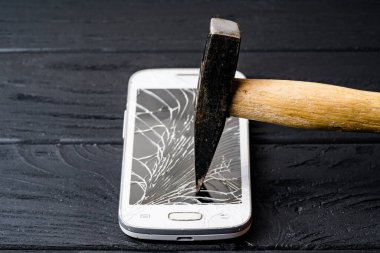 Çekiç, ahşap yüzeyde akıllı telefon ekranına çarpıyor. Bir çekiç, kırık bir ekranı olan akıllı telefonu kırmaya hazırdır.