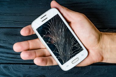Koyu ahşap bir arka planda, elinde duran kırık bir akıllı telefon. Bir el kırık bir ekranla kırık bir akıllı telefonu tutar.