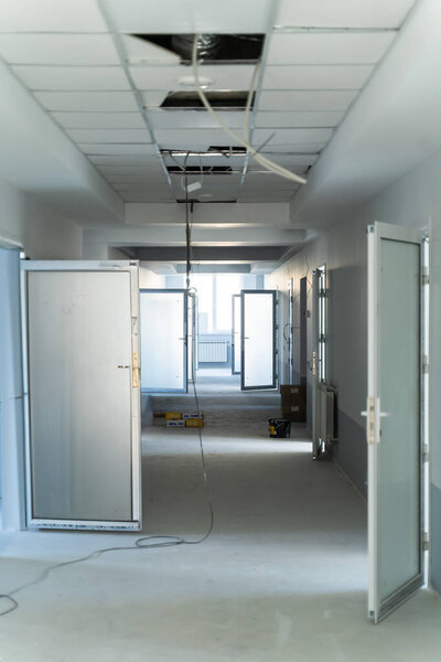 Renovation progress in a hospital corridor under construction. A hospital corridor is under renovation, showcasing unfinished ceilings and doors