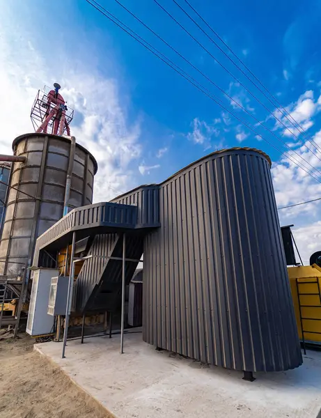 stock image Modern grain storage facility with maintenance worker under blue sky. A maintenance worker inspects a modern grain storage unit under clear blue skies