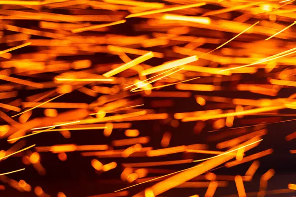 stock image Vibrant sparks flying from metalwork in a dark workshop environment. Bright orange sparks illuminate the air during metalworking