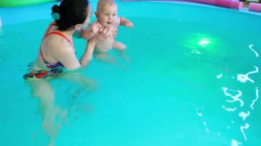 Kadın koç, küçük çocuğu yüzme havuzundaki suya sokuyor. Çocuğa erken yaşta yüzmeyi öğretiyorum..