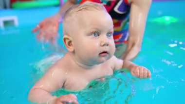 Bebek bezi takan güzel sarışın beyaz bebeğe yüzme öğretildi. Kadın koç bir çocuğun sırtına su sıçratır..