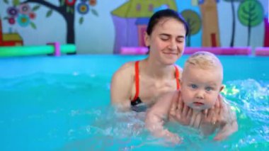 Kadın koç küçük bebeğe yüzmeyi öğretiyor. Kadın, tatlı çocuğu suda bir o yana bir bu yana hareket ettirir..