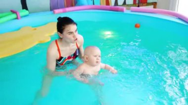 Yüzme havuzunda küçük bir bebeği olan esmer kadın. Hasta kadın yüzme koçu bir çocuğa yüzmeyi öğretiyor..