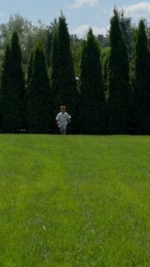 Enerji yüklü beyaz bebek kameraya yaklaşıyor. Mutlu çocuk yazın yumuşak yeşil çimlerin yanından geçiyor. Dikey video.