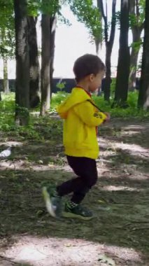 Sarı süveter giyen küçük çocuk güvercinler tarafından çalıştırılıyor. Mutlu aktif bebek yürüyüşünde eğleniyor. Dikey video.