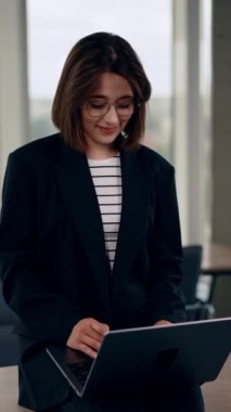 Bilgisayarında daktilo yazan gözlüklü güzel bir beyaz kadın. Kendine güvenen genç bir girişimcinin portresi. Dikey video.