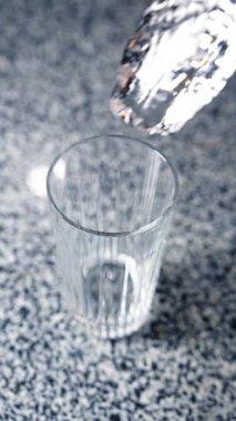 Metal maşayla uzun buz küpü cama yerleştirilir. Masanın üzerinde duran camın üst görüntüsü. İçecek hazırlığı. Dikey video.