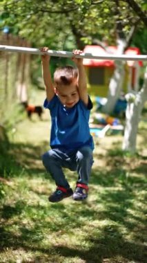 Kafkasyalı neşeli bir çocuk yatay çizgide asılı duruyor ve sallanıyor. Aktif ve sportif büyüyor. Dikey video.