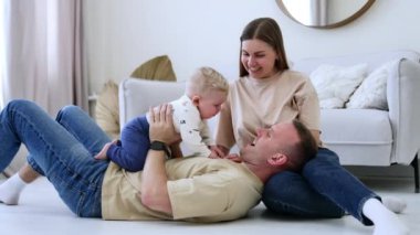 Karısının kucağına uzanmış bir adam bebeğiyle oynuyor. Mutlu aile evde birlikte vakit geçirir..