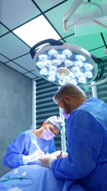 İş arkadaşı erkek ve kadın doktorlar tiroit ameliyatı yaparlar. Tanınmayan ameliyat hemşiresi, aletleri ve malzemeleri doktorun ulaşabileceği bir yere yerleştiriyor. Dikey video.