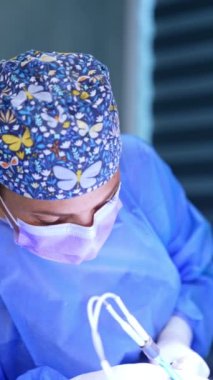Çiçekli ve kelebekli şapka takan kadın cerrah ameliyat yapıyor. Doktor çalışmalarında modern elektrikli cerrahi aletler kullanıyor. Dikey video.
