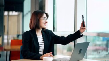 Akıllı telefondan ya da canlı yayında görüntülü sohbet. Esmer, video veya selfie çekmek için cihaz kullanarak masada oturuyor..