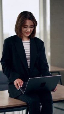 Masanın üzerinde kendiliğinden beyaz bir kadın oturuyordu. Laptopa bakan gülümseyen kız konsantre oldu. Dikey video.