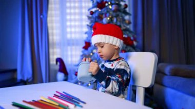 Noel Baba şapkalı beyaz çocuk komik mavi bardaktan içiyor. Güzel çocuk Noel 'i kutluyor.