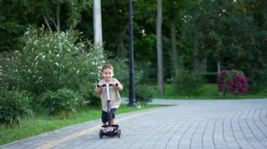 Güzel, gülümseyen bir bebek motosikletiyle kameraya yaklaşıyor. Tatlı çocuk yazın güzel parkta aktif vakit geçiriyor..