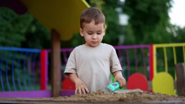Kum havuzunda duran sevimli beyaz bebek. Çocuk yazın parkta kumla oynuyor..