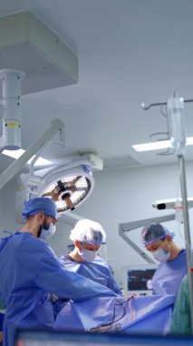 Mavi üniformalı ve maskeli cerrahlar ameliyat masasında bekliyor. Ön planda eğri çizgiler olan bilgisayar ekranındaki odaklanma düğmeleri. Dikey video.