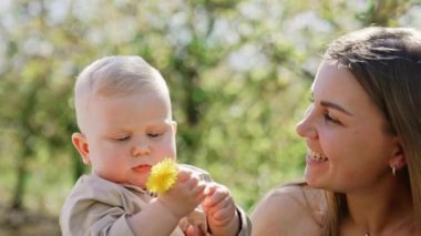 Anne, baba ve küçük bebek güneşli bir günde dışarıda beraberler. Kafkasyalı çift sevgili çocuklarını yanaklarından öpüyor. Elinde çiçek tutan bir çocuk. Kapat..