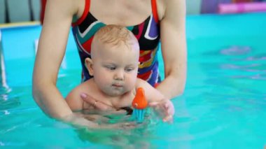 Suyun içinde oyuncak tutan güzel sarışın bebek. Sevimli çocuk yüzme havuzunda yüzmeyi öğreniyor. Kapat..