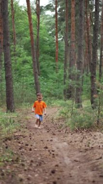 Sevimli mutlu çocuk kameraya doğru koşuyor. Gülümseyen çocuk ormanda çıplak ayakla yürüyor. Dikey video.