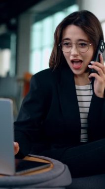 Güzel, beyaz bir kadın telefonunu kulağına dayayıp dizüstü bilgisayarına bakıyor. Hanımefendiye şaşırtıcı bir haber geliyor ve kafası karışmış görünüyor. Dikey video.