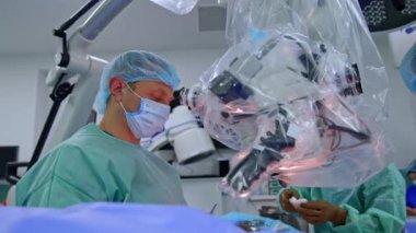 Erkek doktorlar ameliyat masasında asılı mikroskoba bakarlar. Nöroşirürji operasyonu devam ediyor.