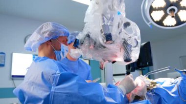 Hastanın başında oturan profesyonel erkek cerrah beyin ameliyatı yapıyor. Doktor mikroskop taşıma operasyonuna bakıyor..