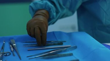 El, kahverengi lateks eldivenli tanınmayan sıhhiyeye, metal aletleri cerrahi standında hareket ettiriyor. Operasyon için araç gereç ayarlanıyor. Kapat..