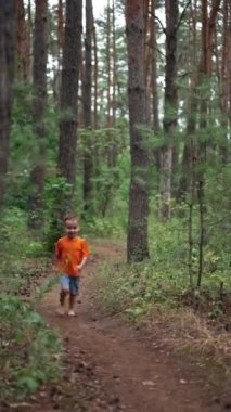 Neşeli beyaz çocuk kameraya doğru koşuyor. Yazın ormanda çıplak ayaklı mutlu bir çocuk. Dikey video.
