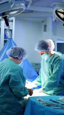 Ameliyat masasının üstünde iki kadın doktor var. Cerrah büyük bir şırınga kullanır ve ameliyat hemşiresine verir. Dikey video.