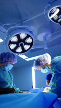 Kadın sıhhiyeciler hastanın iki tarafında dururlar. Doktor bir ameliyat hemşiresinin yardımıyla ameliyat yapıyor. Düşük açı. Dikey video.