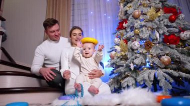 Mutlu Kafkas ailesi Noel ağacının önünde yerde oturuyor. Annem oyuncakları çocuğun kafasına koyuyor. Düşük açı görünümü.