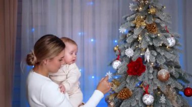 Anne güzel dekore edilmiş Noel ağacını küçük bebeğine gösteriyor. Anne ve oğlu tatilleri birlikte kutluyor..