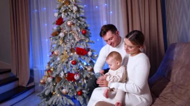 Kafkasyalı anne ve baba oturma odasındaki kanepede oturuyorlar. Ebeveynler sevgili bebeklerinin bir oyuncakla oynamasına bakarlar. Arkaplanda Noel ağacı.