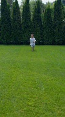 Mutlu çıplak ayaklı beyaz çocuk yeşil çimlerin yanında koşuyor. Enerjik çocuk yazın dışarıda eğleniyor. Dikey video.