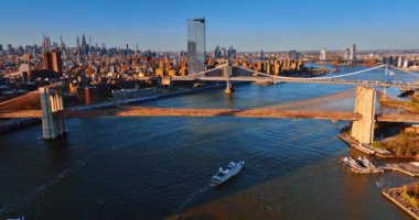 Doğu Nehri üzerindeki köprülerde ve New York binalarının cephelerinde güneşin batışının sıcacık ışığı. Gün batımında metropolde hava perspektifi.