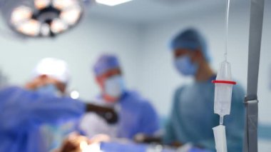 Damardan ilaç damlatılıyor. Ekipman ameliyathanede. Doktorlar arka planda bulanık çalışırlar..