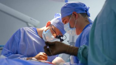 Cerrahi hoparlör takan konsantre cerrah operasyonda metal alet kullanıyor. Tanınmayan hemşire enstrümanı doktora veriyor. Düşük açı görünümü.