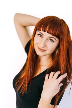 Beyaz arka planda uzun kızıl saçlı, kendine güvenen genç bir kadın. Canlı kızıl saçlı bir kadın neşeli bir poz verir. Tarzını ve cazibesini parlak bir ortamda sergiler..