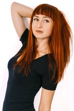 Beyaz bir arkaplanda poz veren kendine güvenen kızıl saçlı kadın. Canlı kızıl saçlı bir kadın, elleri başının arkasında rahatça poz verir.