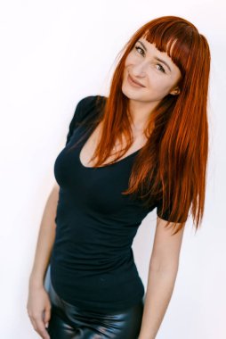 Siyahlı, uzun kızıl saçlı genç kadın beyaza poz veriyor. Kızıl saçlı genç bir kadın kendine güvenen bir poz veriyor, siyah bir bluz giyiyor.