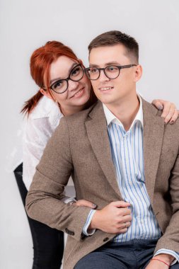 Tarafsız bir zemine karşı birlikte poz veren şık bir çift. Gülümseyen bir çift şık kıyafetler içinde poz verirken, aşklarını ve ilişkilerini ışık dolu bir ortamda sergilerler..