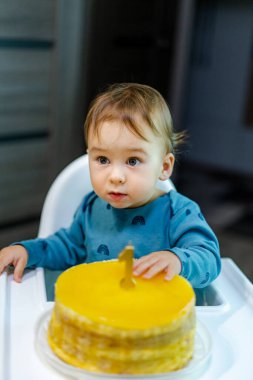 Yeni yürümeye başlayan çocuğun ilk doğum gününde sarı pasta! Küçük bir çocuk ilk doğum günlerini heyecan ve merakla kutlayan sarı bir doğum günü pastasına uzanır..