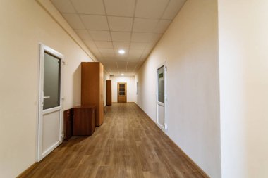 Ahşap döşemeleri ve ofis kapıları olan uzun bir koridor. İyi aydınlatılmış bir koridorda ahşap döşemeler ve ofislere açılan birden fazla kapı bulunur.